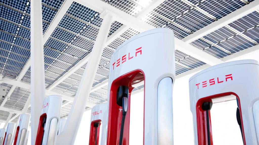 A row of tesla chargers in front of a solar panel.