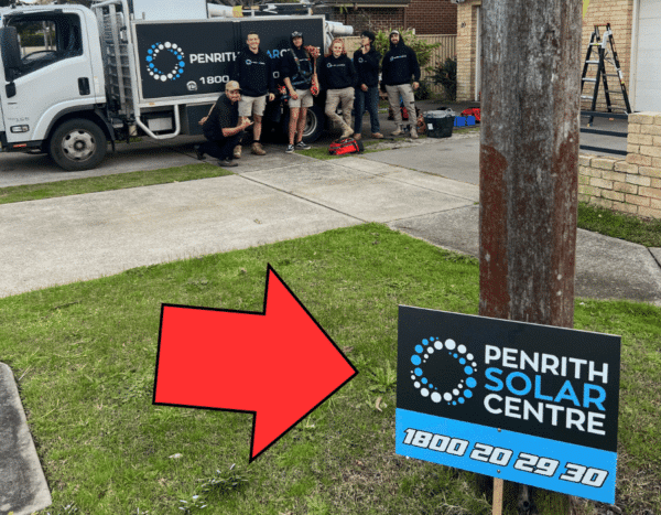 A group of five people stands near a work truck labeled "Penrith Solar Centre." A sign in the foreground displays the same name and phone number. A red arrow points to the sign.