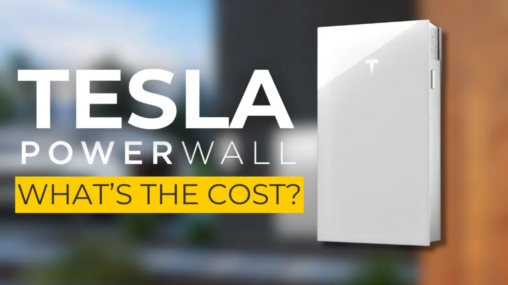 Image of a Tesla Powerwall battery mounted on a wall with the text "TESLA POWERWALL WHAT'S THE COST?" in bold white and yellow letters. Blurry outdoor background.