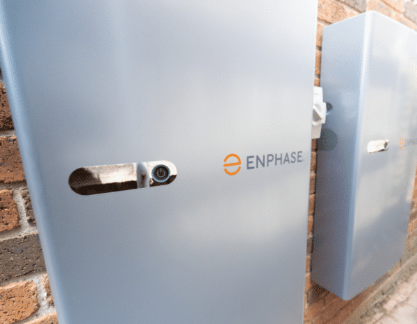 Close-up of two Enphase energy storage systems mounted on a brick wall. The Enphase logo is visible on both units.