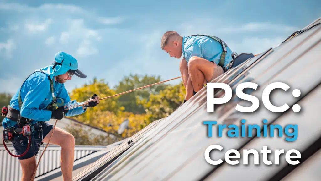 Two individuals equipped with safety gear, including harnesses and helmets, practice rooftop work skills at the PSC Training Centre on a sunny day.