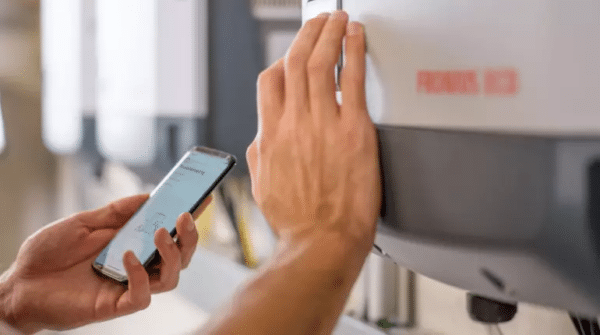 Person holding a smartphone while adjusting a setting on an industrial machine labeled FRONIUS.