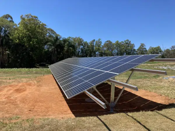 A solar panel installation on the ground in a clear area with trees in the background under a clear blue sky.