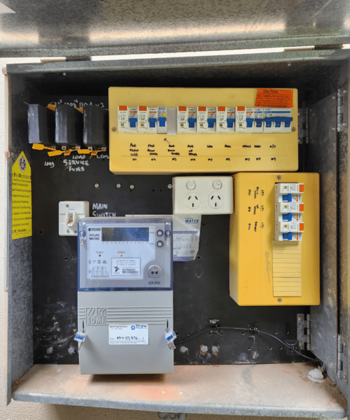 Electrical panel box with labeled fuse switches, a digital meter, and wall outlets.