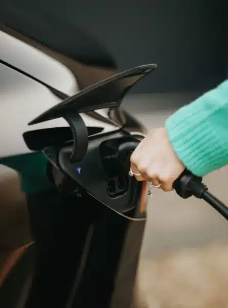 A person in a green sweater plugs a charger into an electric car.