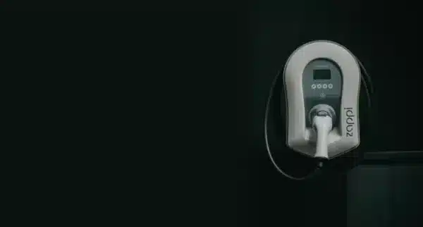 A wall-mounted electric vehicle charger with a coiled charging cable is installed on a dark background. The brand "zappi" is visible on the charger.